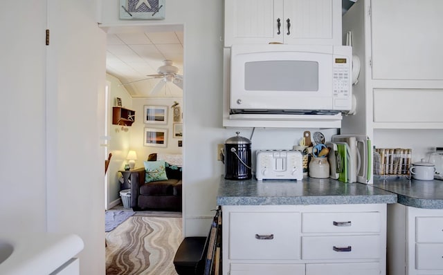 kitchen with dark countertops, white microwave, white cabinets, and a ceiling fan