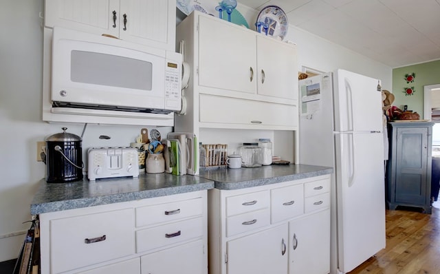 kitchen featuring dark countertops, white appliances, white cabinetry, and wood finished floors