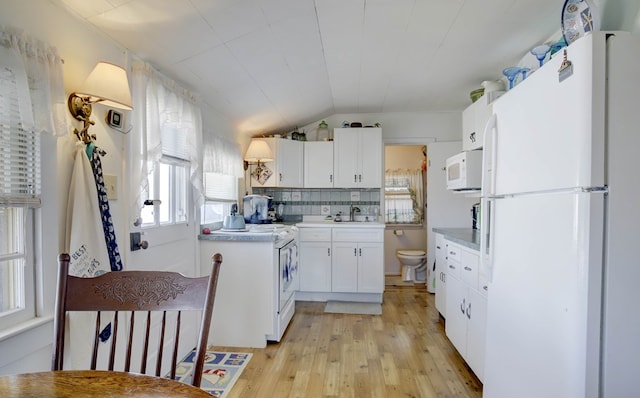 kitchen with white appliances, light wood finished floors, vaulted ceiling, white cabinetry, and backsplash