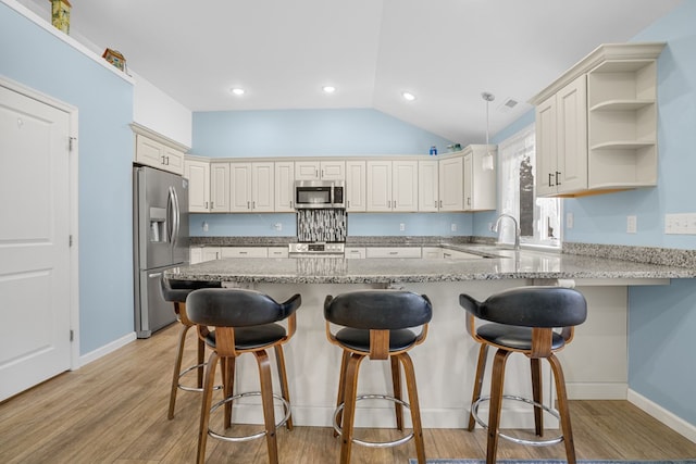 kitchen featuring appliances with stainless steel finishes, a peninsula, light stone countertops, vaulted ceiling, and light wood-type flooring