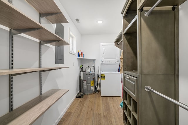 spacious closet featuring stacked washer and dryer, visible vents, electric water heater, wood finished floors, and electric panel