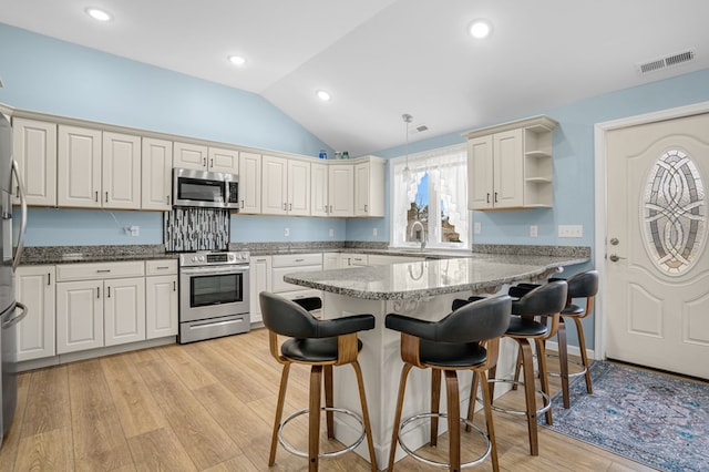 kitchen featuring light wood-style flooring, a breakfast bar, visible vents, vaulted ceiling, and appliances with stainless steel finishes