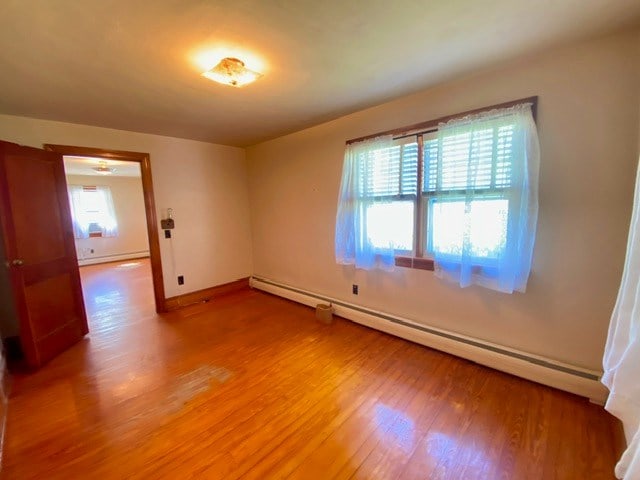 empty room featuring baseboards, light wood-style floors, and a baseboard radiator