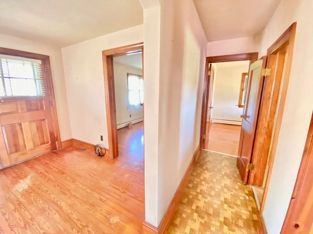 hall featuring a baseboard heating unit, baseboards, and light wood finished floors