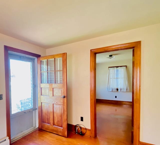 doorway with a baseboard heating unit, wood finished floors, a healthy amount of sunlight, and baseboards