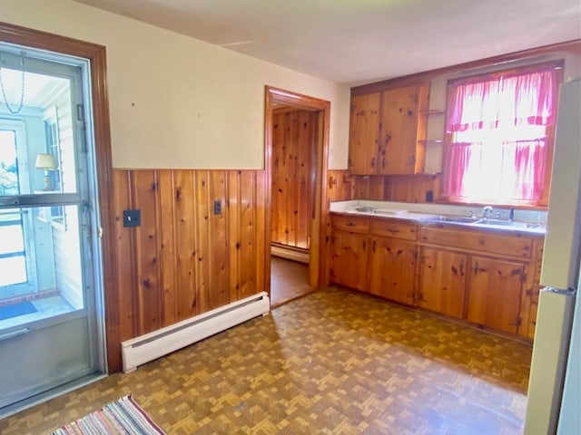 kitchen featuring wainscoting, baseboard heating, a sink, and brown cabinets