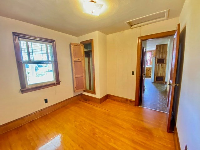 unfurnished room with attic access, light wood-style floors, and baseboards