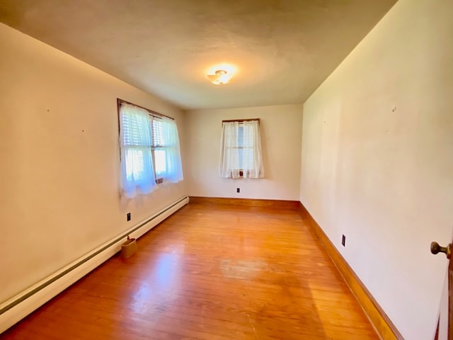 spare room with a baseboard heating unit, light wood finished floors, and baseboards