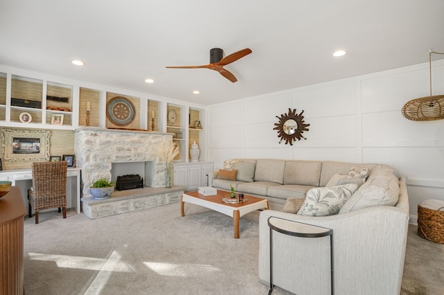 carpeted living area with a decorative wall, built in shelves, ceiling fan, and a premium fireplace