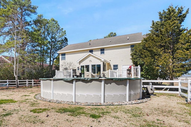 rear view of property with an outdoor pool, a wooden deck, a yard, and fence