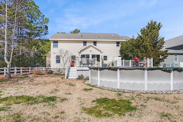 rear view of house with an outdoor pool, a wooden deck, and fence