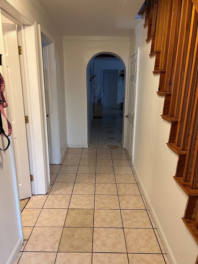 hall with arched walkways, a textured ceiling, baseboards, and light tile patterned floors