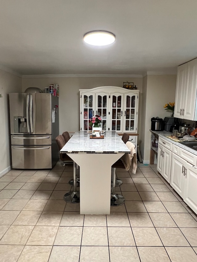 kitchen featuring white cabinets, light tile patterned floors, stainless steel refrigerator with ice dispenser, and a kitchen breakfast bar