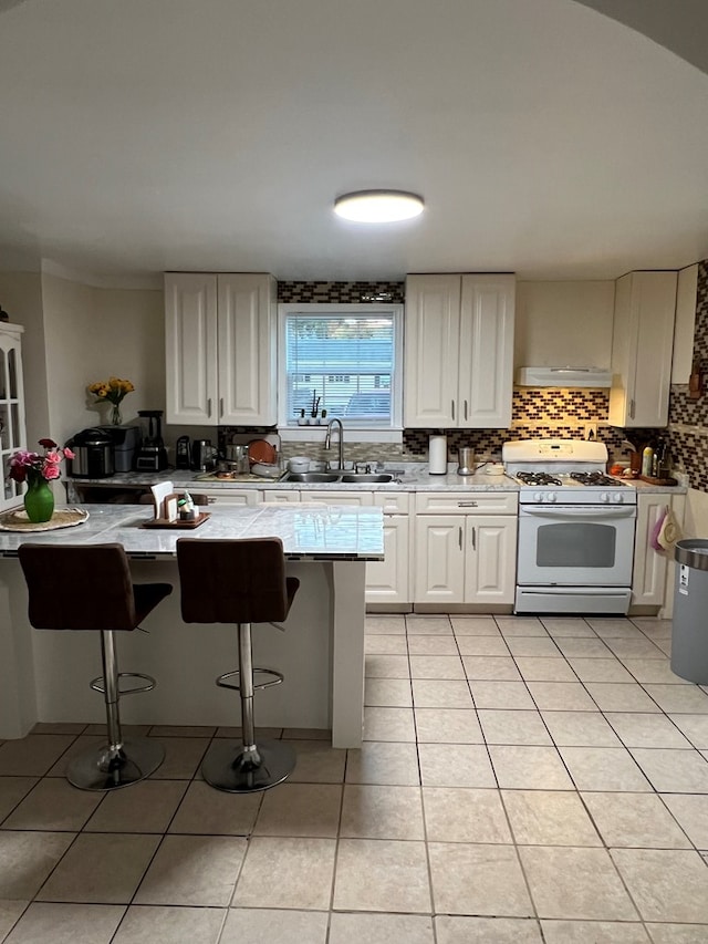 kitchen featuring decorative backsplash, a sink, white gas range oven, a kitchen breakfast bar, and exhaust hood