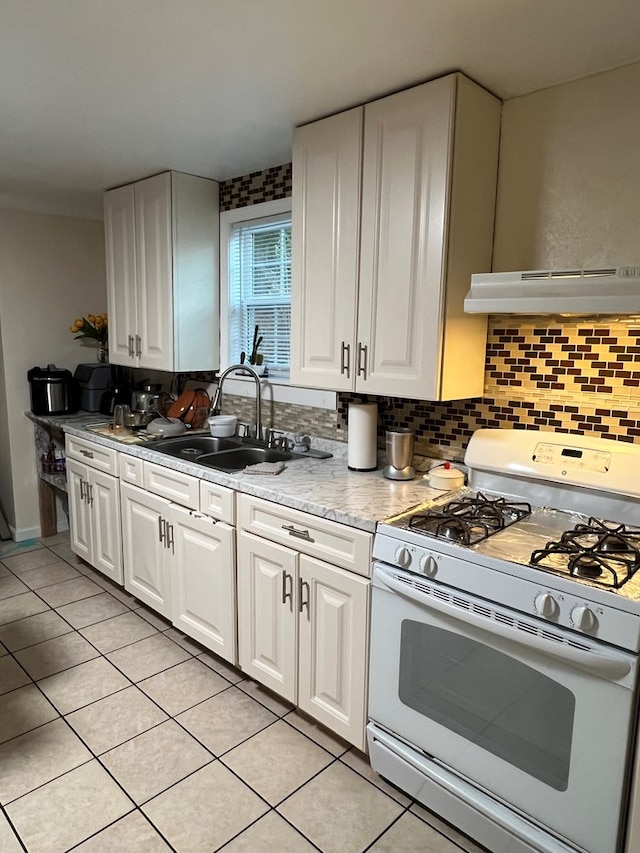 kitchen featuring white gas stove, backsplash, white cabinetry, a sink, and under cabinet range hood