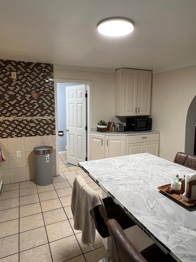 kitchen featuring light tile patterned floors, black microwave, light countertops, white cabinetry, and tile walls