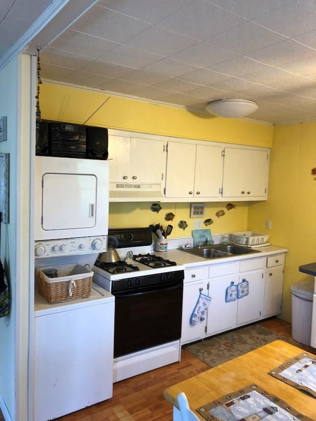 2561 Captains Corridor, Greenbackville, VA 23356 - kitchen with range with gas cooktop, under cabinet range hood, stacked washer / dryer, white cabinetry, and light wood finished floors