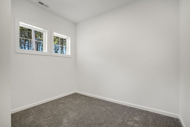 empty room featuring visible vents, baseboards, and dark colored carpet