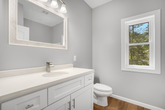bathroom featuring vanity, toilet, baseboards, wood finished floors, and visible vents