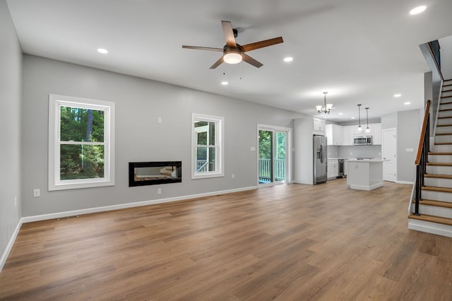 unfurnished living room featuring recessed lighting, ceiling fan with notable chandelier, visible vents, and stairway