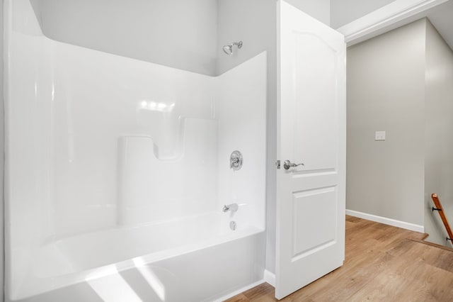 bathroom featuring baseboards, wood finished floors, and tub / shower combination