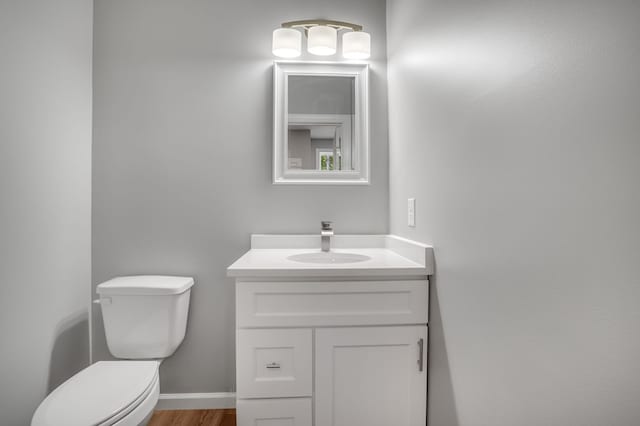 half bathroom with vanity, toilet, and wood finished floors