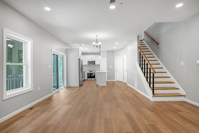 unfurnished living room with recessed lighting, visible vents, light wood-style flooring, and stairway