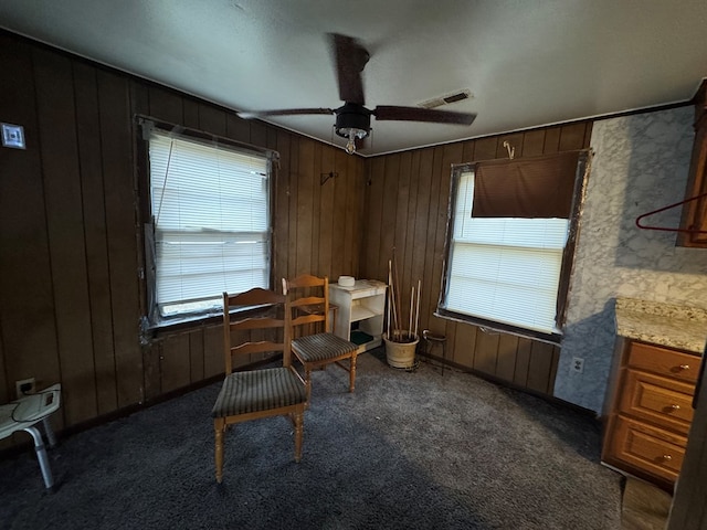 sitting room with dark colored carpet, ceiling fan, and wood walls