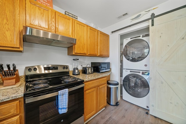 kitchen with appliances with stainless steel finishes, a barn door, stacked washing maching and dryer, under cabinet range hood, and visible vents