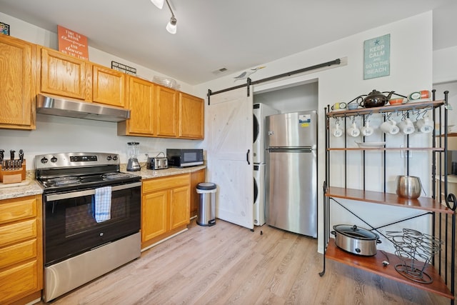 kitchen featuring visible vents, appliances with stainless steel finishes, stacked washer / drying machine, light wood-style floors, and under cabinet range hood