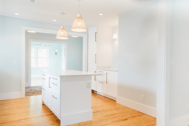 kitchen with light countertops, light wood-style flooring, white cabinetry, decorative light fixtures, and a kitchen island