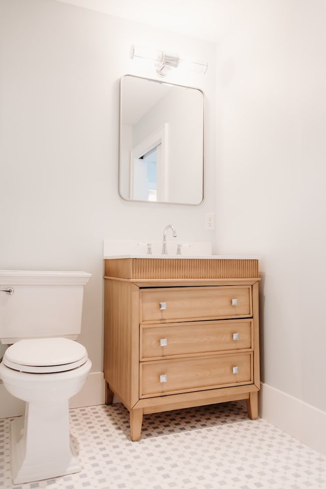half bath with toilet, baseboards, and vanity