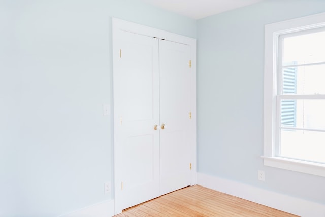 unfurnished bedroom with baseboards, multiple windows, a closet, and light wood finished floors