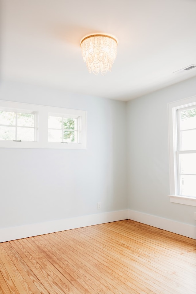 spare room with baseboards, an inviting chandelier, wood finished floors, and visible vents
