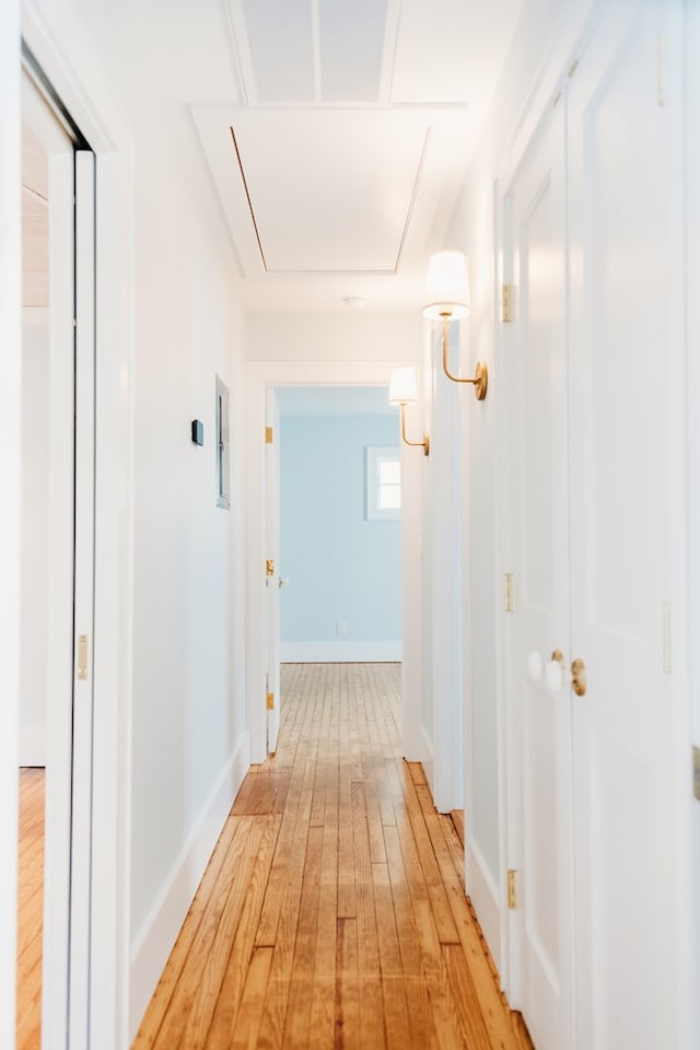 hall with baseboards, attic access, and light wood-style flooring