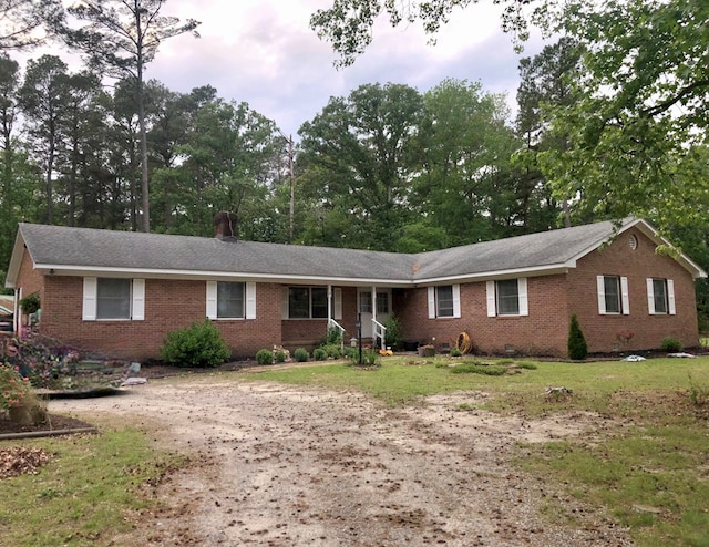 21020 Adams Rd, Greenbush, VA 23357 - ranch-style home featuring brick siding, driveway, a front lawn, and view of wooded area