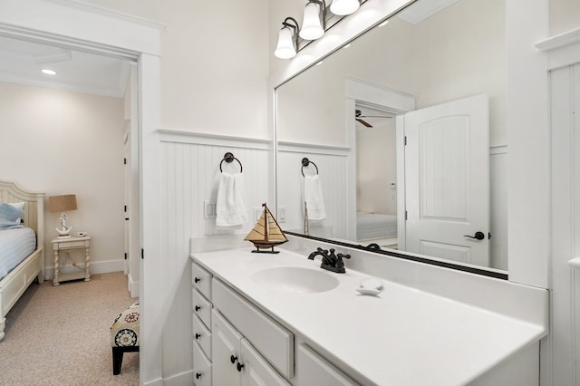 ensuite bathroom with vanity, a ceiling fan, ornamental molding, wainscoting, and connected bathroom