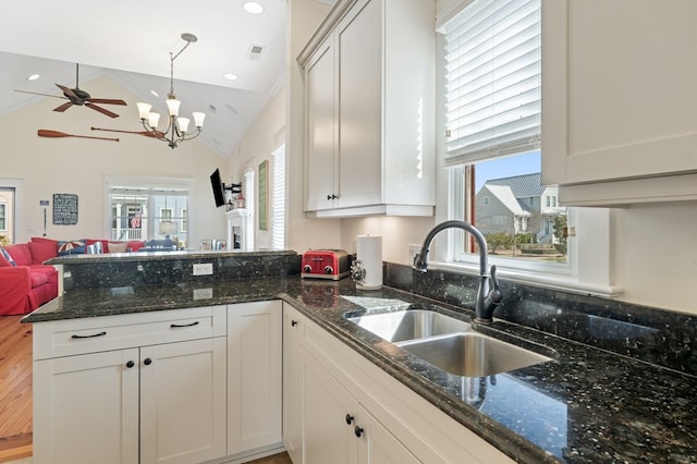 kitchen with dark stone countertops, a peninsula, a sink, ceiling fan with notable chandelier, and open floor plan