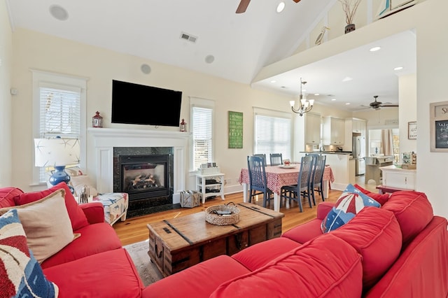 living area featuring ceiling fan with notable chandelier, lofted ceiling, light wood-style floors, and a premium fireplace