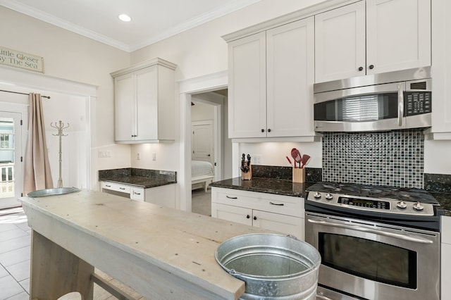 kitchen featuring backsplash, crown molding, dark stone counters, light tile patterned floors, and appliances with stainless steel finishes