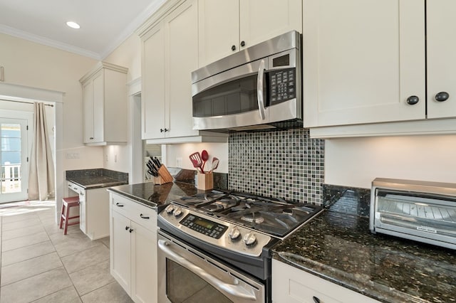 kitchen featuring light tile patterned floors, dark stone counters, ornamental molding, appliances with stainless steel finishes, and tasteful backsplash