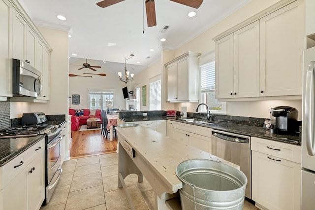 kitchen featuring light tile patterned flooring, a sink, stainless steel appliances, crown molding, and ceiling fan with notable chandelier