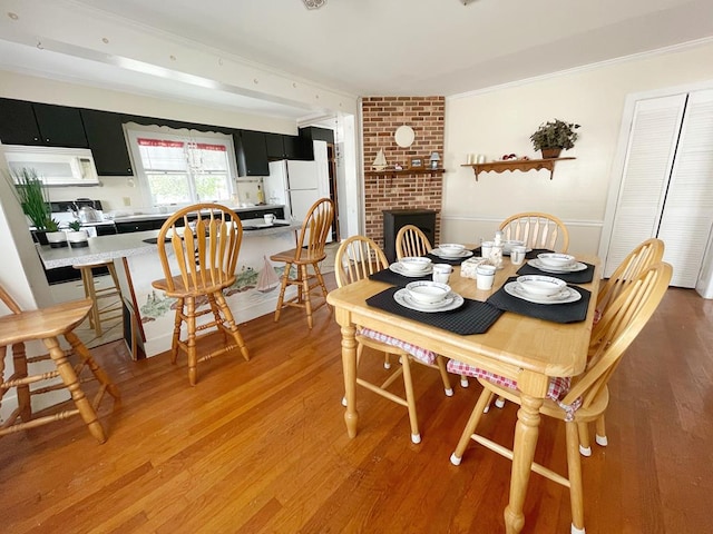 dining area with hardwood / wood-style flooring, ornamental molding, and a brick fireplace