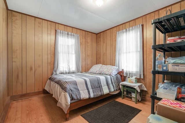 bedroom with multiple windows, wood walls, and light wood-type flooring
