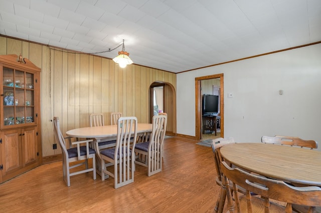 dining space with wood walls, light hardwood / wood-style floors, and crown molding
