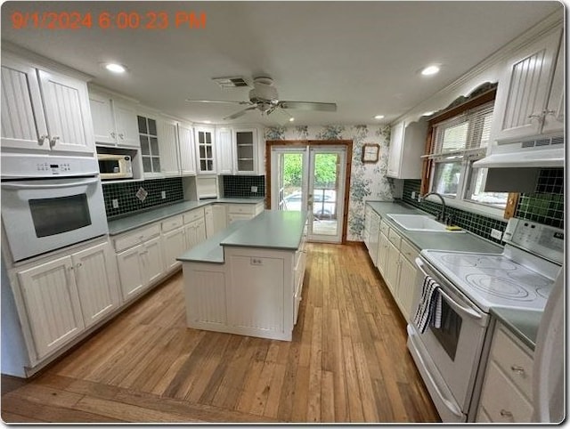 kitchen with exhaust hood, white appliances, white cabinetry, and sink