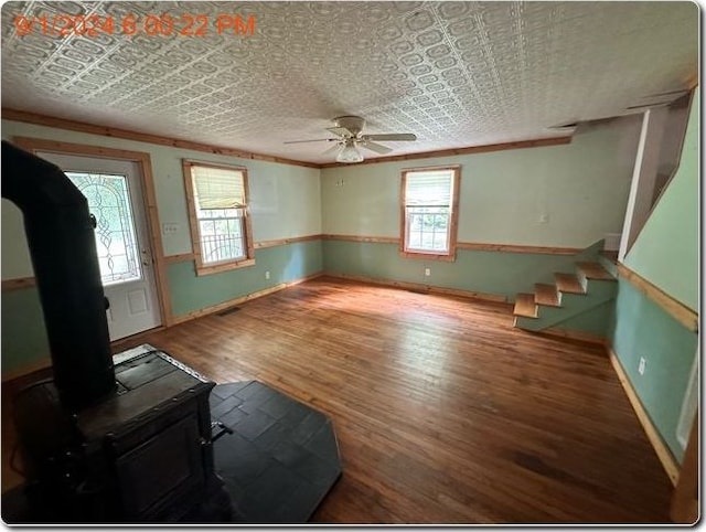 unfurnished living room with a wood stove, ceiling fan, ornamental molding, and hardwood / wood-style flooring