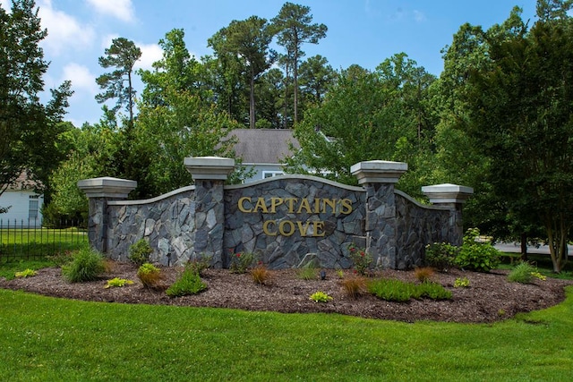 community / neighborhood sign featuring a yard and fence
