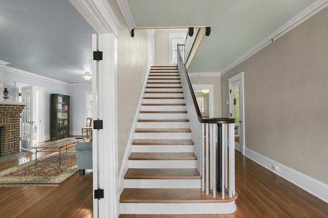 staircase with ornamental molding, a brick fireplace, baseboards, and wood finished floors