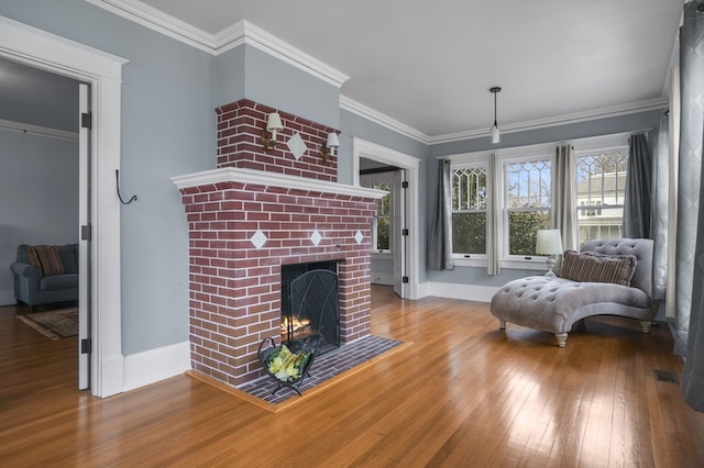 living area featuring a brick fireplace, baseboards, crown molding, and wood finished floors